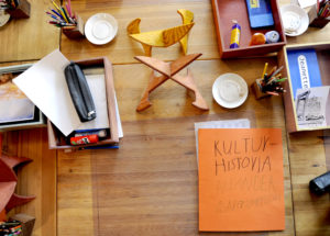 Skolmiljö som visar ett skrivbord med elevens studiematerial på en anpassad gymnasieskola (gymnasiesärskola) i Järna. Bok med texten "Kulturhistoria".