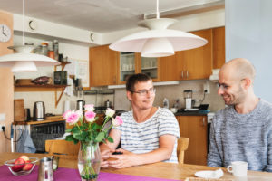 Två personer dricker kaffe, sittandes vid ett matbord, i köket på ett LSS boende.